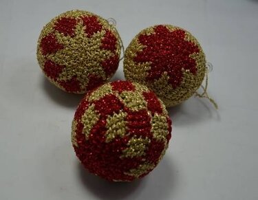 Drei gehäkelte Kugeln in Rot und Gold mit sternförmigem Muster auf hellem Untergrund.
