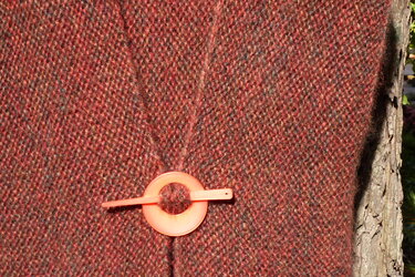 Nahaufnahme einer rostroten gestrickten Jacke mit rundem orangen Schließring