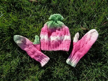 Gestricktes Mützen- und Fäustlings-Set in Rosa, Weiß und Grün auf Gras