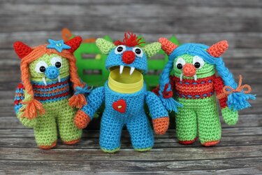 Drei gehäkelte Monster-Amigurumis, das blaue in der Mitte ist geöffnet und zeigt eine gelbe Plastikkapsel.