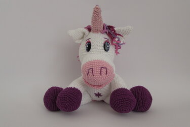 weißes gehäkeltes Einhorn-Amigurumi mit rosa Schnauze und lila Hufen