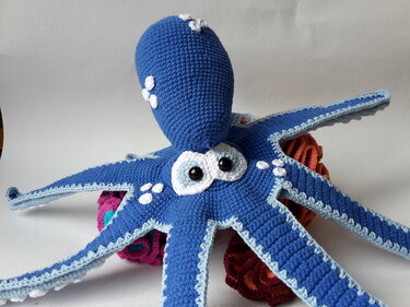 Nahaufnahme eines blau gehäkelten Oktopus-Amigurumi mit deutlich sichtbaren Maschen und weißen Applikationen