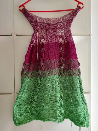 Gehäkelte ärmellose Tunika in abgestuften Pink- und Grüntönen mit vertikalen Lochmustern, an einem roten Kleiderbügel hängend
