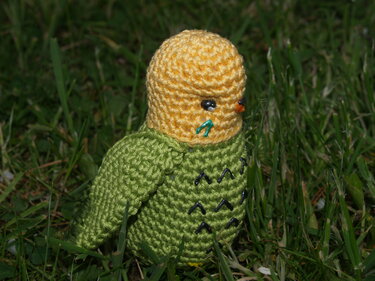 Gehäkelter Amigurumi-Vogel mit gelbem Kopf und grünem Körper im Gras