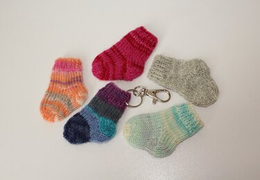 Fünf winzige gestrickte Babysöckchen in verschiedenen Farben, eines davon mit Metall-Karabiner und Schlüsselring