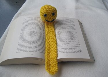 Gelbes gestricktes Lesezeichen mit rundem Smiley-Kopf auf offenem Buch