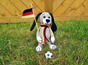 Gehäkelter Amigurumi-Hund mit Deutschlandflagge und Fußball auf Wiese