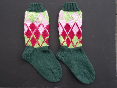 Paar gestrickter Socken mit dunkelgrünem Fuß und mehrfarbigem Rautenmuster in Rot, Rosa und Hellgrün