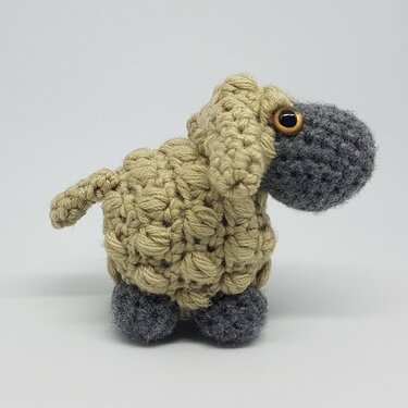 Gehäkeltes Amigurumi-Schaf mit sandfarbenem Noppenmusterkörper und grauem Kopf.