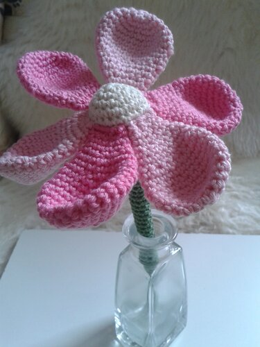 Gehäkelte Blume mit becherförmigen Blütenblättern und grünem Stiel in einer kleinen Glasvase