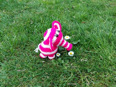 Gehäkelter pink-weiß gestreifter Amigurumi-Elefant im Gras mit Gänseblümchen