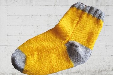 Handgestrickte gelbe Socke mit grauen Bündchen, Ferse und Spitze auf hellem Hintergrund.