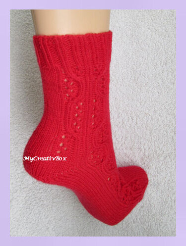 Rote handgestrickte Socke auf Fußform mit Ajour- und Zopfmuster