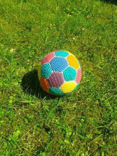 Handgehäkelter Ball mit bunten Sechsecken auf grünem Gras
