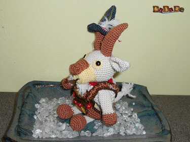 Gehäkelte Amigurumi-Ziege mit braunen Hörnern und dunkelblauem Hut in blauer Schale