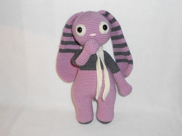Gehäkelter fliederfarbener Amigurumi-Hase mit langen gestreiften Ohren, Sicherheitsaugen und hellem Schal, stehende Pose