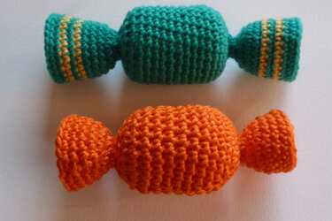 Zwei gehäkelte Katzenspielzeuge in Bonbonform, grün mit gelben Streifen und orange