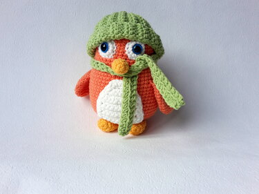 Gehäkelter orange-weißer Amigurumi-Vogel mit grüner Mütze und Schal