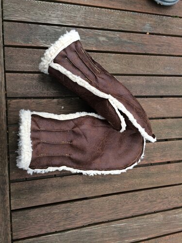 Nahaufnahme von braunen Fäustlingen mit weißem Kunstfellbesatz auf Holz.