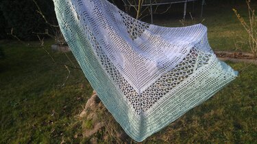 Gehäkeltes Dreieckstuch mit Hellblau-zu-Mintgrün-Verlauf und Spitzen-Gittermuster, an einem Zweig im Freien aufgehängt.