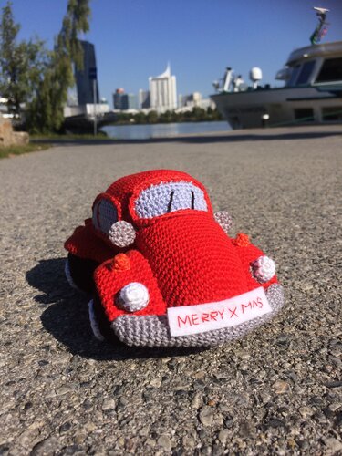 Rotes gehäkeltes Amigurumi-Auto mit weißem 'Merry X Mas'-Schild auf Asphalt