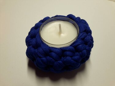 Teelicht in einem dunkelblau gehäkelten Körbchen aus dickem Stoffgarn auf hellem Untergrund