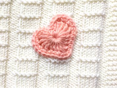 weiße gestrickte Babydecke im Karo-Muster mit kleinem rosa gehäkeltem Herz