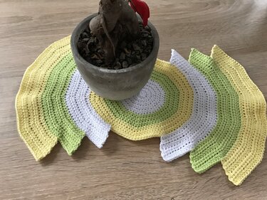 Gehäkeltes halbrundes Deckchen in Gelb, Hellgrün und Weiß unter einem Blumentopf