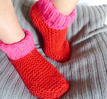 Zweifarbige rot-pinke gestrickte Sockenpantoffeln auf grauer Strickdecke
