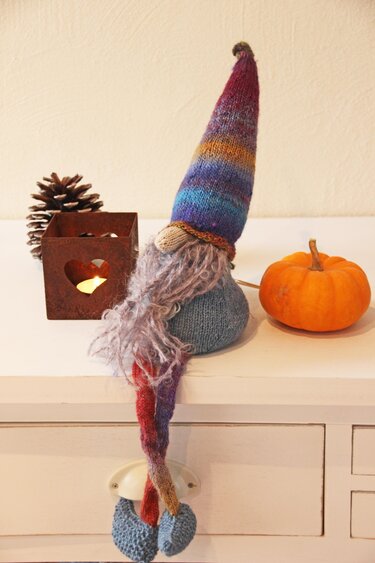 bunter gestrickter wichtel mit langer zipfelmütze und gewelltem bart auf sideboard neben kürbis