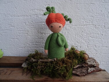 Gehäkelte Amigurumi-Puppe mit orangefarbener Haube und grünem Kleid auf Moos