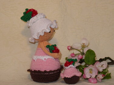 Zweier-Set gehäkelter Amigurumi-Puppen mit Rüschen, Erdbeeren und brauner Cupcake-Basis neben blühendem Zweig