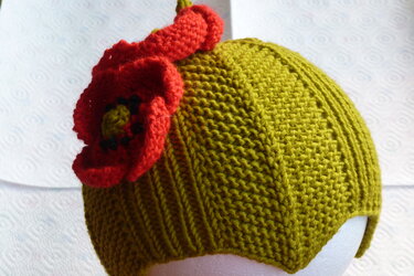 Gestrickte olivgrüne Kindermütze mit roter Mohnblume auf weißem Hintergrund