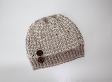 Melierte beige-weiße Babymütze aus Strick mit zwei dunklen Knöpfen am Bündchen
