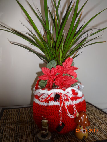 Zimmerpflanze in rot-weißem, gehäkeltem Übertopf mit roten Weihnachtssternen und kleinen Dekofiguren