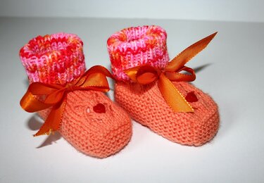 Paar gestrickte Babyschuhe in Rosa und Orange mit melierten Bündchen, Schleifenbändern und kleiner Herz-Applikation