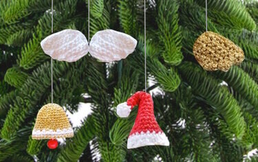 Handgehäkelte Weihnachtsornamente (rote Mütze, goldene Glocke, weiße Formen) an Tannenzweigen