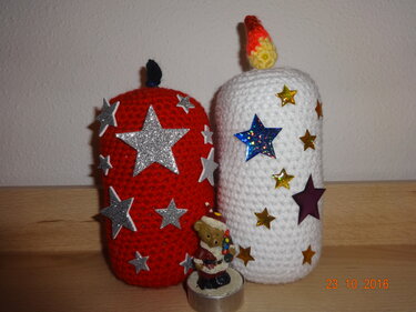 Zwei gehäkelte Kerzendekorationen in Rot und Weiß mit glitzernden Sternaufklebern und einer kleinen Bären-Teelichtfigur davor