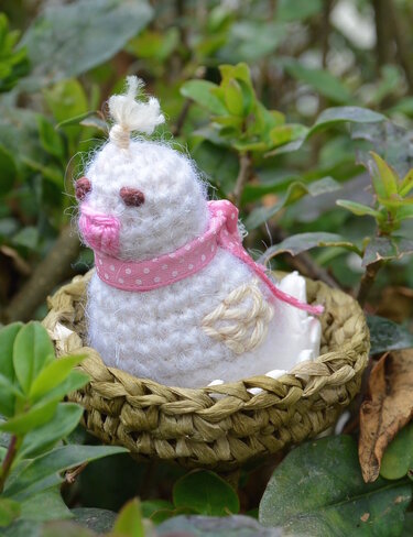 Weißer gehäkelter Amigurumi-Vogel mit rosa Schleife im kleinen geflochtenen Nest