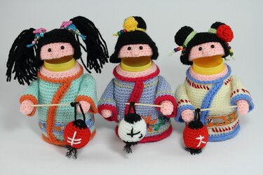 Drei gehäkelte Amigurumi-Puppen in bunten Outfits mit Mini-Laternen