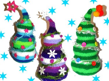 Drei gehäkelte, kegelförmige Weihnachtsbäume in grünen, lila und weißen Streifen, dekoriert mit Knöpfen, Sternen und Ziergarn vor weißem Hintergrund mit blauen Sternen