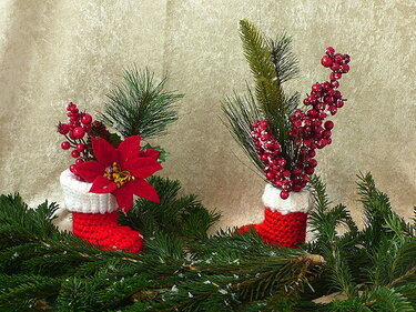 Zwei gehäkelte rot-weiße Mini-Weihnachtsstiefel gefüllt mit Weihnachtsstern, roten Beeren und Tannenzweigen auf Tannengrün