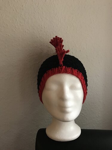 Schwarz-rote Strickmütze mit rotem Zierelement auf Styroporkopf