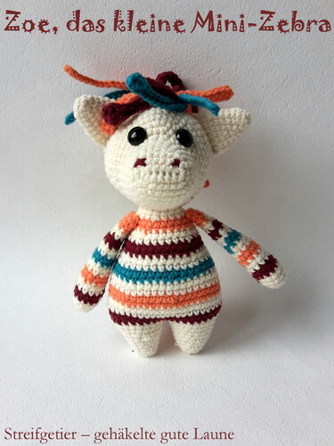 Gehäkeltes Amigurumi-Mini-Zebra mit bunten Streifen (Orange, Dunkelrot, Türkis), schwarzen Knopfaugen und farbiger Mähne.