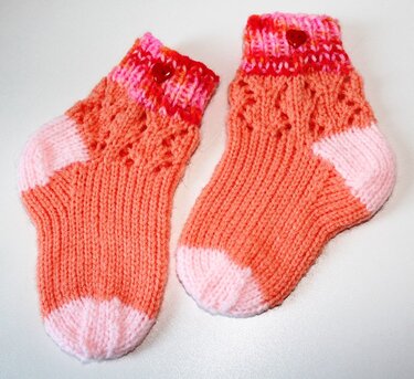 Gestrickte Babysocken in Koralle mit rosa Zehen und herzförmigen Knöpfen