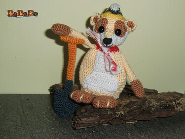 Gehäkeltes Amigurumi-Tier sitzend mit Schleife, Häubchen und gehäkelter Schaufel