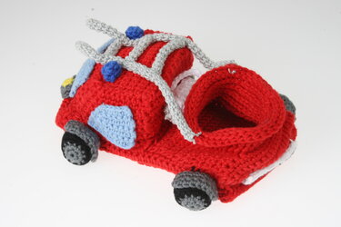 Rote gehäkelte Babyschuhe im Feuerwehrauto-Design mit grauen Leiterstangen und blauen Applikationen auf weißem Hintergrund.