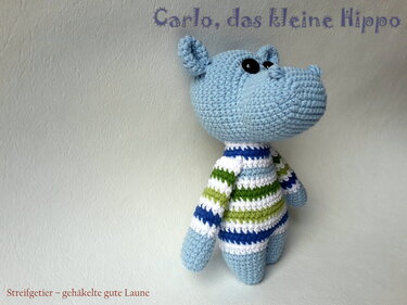 Hellblaues gehäkeltes Nilpferd Amigurumi mit blau-grün-weiß gestreiftem Pullover.