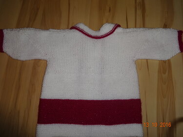Gestrickte weiße Babyjacke mit breitem roten Saum und roten Bündchen, flach auf Holz