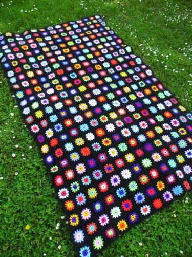 Gehäkelte Granny-Squares-Decke mit bunten Blumen auf Gras